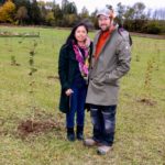A couple poses in a grassy field, with trees in the background,