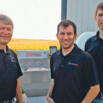 Praxidyn founder Doug Applegate with sons Luke, at left, and Brent focus their energy on developing products like their Mixmate Pro Inductor, in the background, to help streamline the process of filling sprayers.