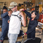 Abisola Omoniyi and Ornwipa Thamsuwan from the Canadian Centre for Health and Safety in Agriculture at the University of Saskatchewan hook an exoskeleton to Ron Swan of Glenside, Sask., who volunteered to test the unit on the farm.