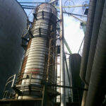 A close-up of a commercial grain dryer with multiple levels, pipes, and platforms, used to dry grain efficiently after harvest