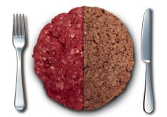 A close-up of a burger patty cut in half, revealing one side made from ground beef and the other side made from a plant-based meat alternative.