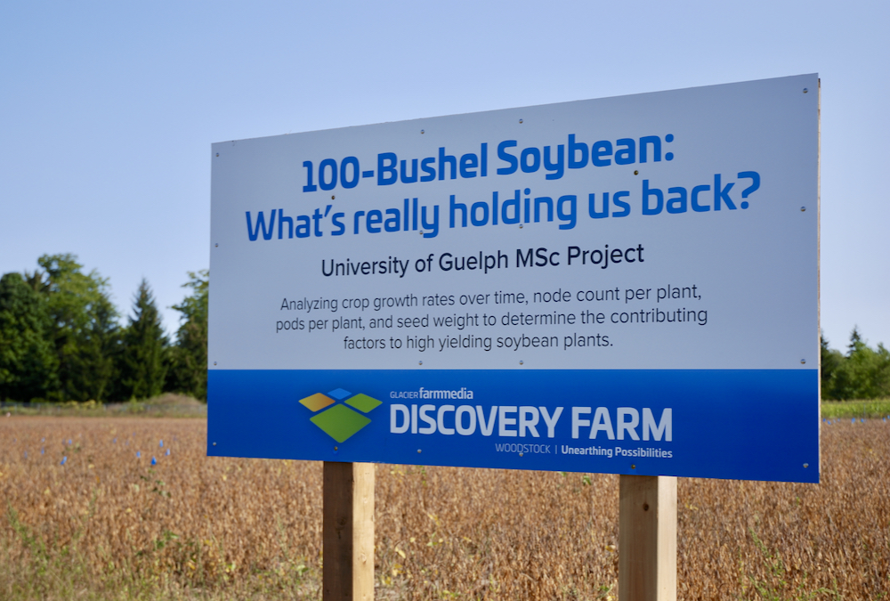 A sign reading "100 Bushels of Soybean" set against a backdrop of soybean crops
