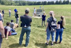 Rick Kootstra (blue shirt) and Mari Veliz (white shirt, orange hat) explaining the field-edge water monitoring station in a pattern-tile drainage field at a Soil Health Water Quality Field Day on June 21.