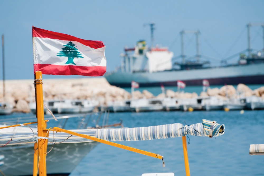 File photo of a small boat flying the Lebanese flag at a marina in Tripoli as a cargo vessel sails in the distance. (Joel Carillet/iStock/Getty Images)
