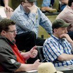 Two men sitting beside each other use subtle hand gestures to indicate their bids