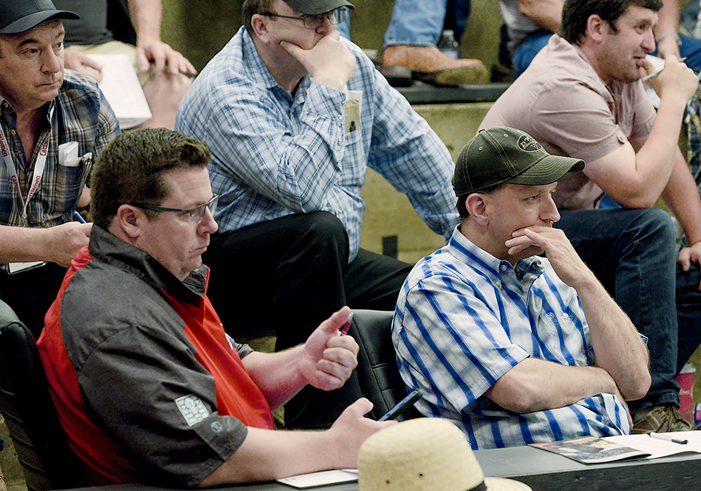 Two men sitting beside each other use subtle hand gestures to indicate their bids