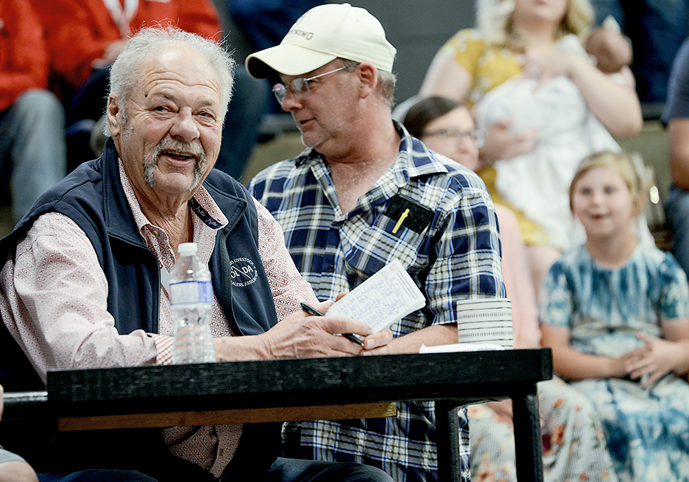 A man sitting at a table grins widely after winning a hard and fast bidding war.