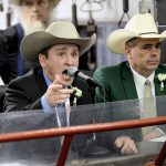 An auctioneer wearing a cowboy hat points to a bid while chanting into a microphone during a cattle auction