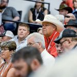 A man in a cream coloured cowboy hat and strong red shirt sits a head above those around him, watching the auctioneers