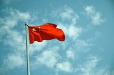 The Chinese flag flying against a blue sky with white clouds.