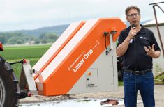 Chuck Baresich, Haggerty AgRobotics, stands beside a bright orange Pixelfarming Laser One–i prototype adapted to fit the Orio NAiO’s frame.