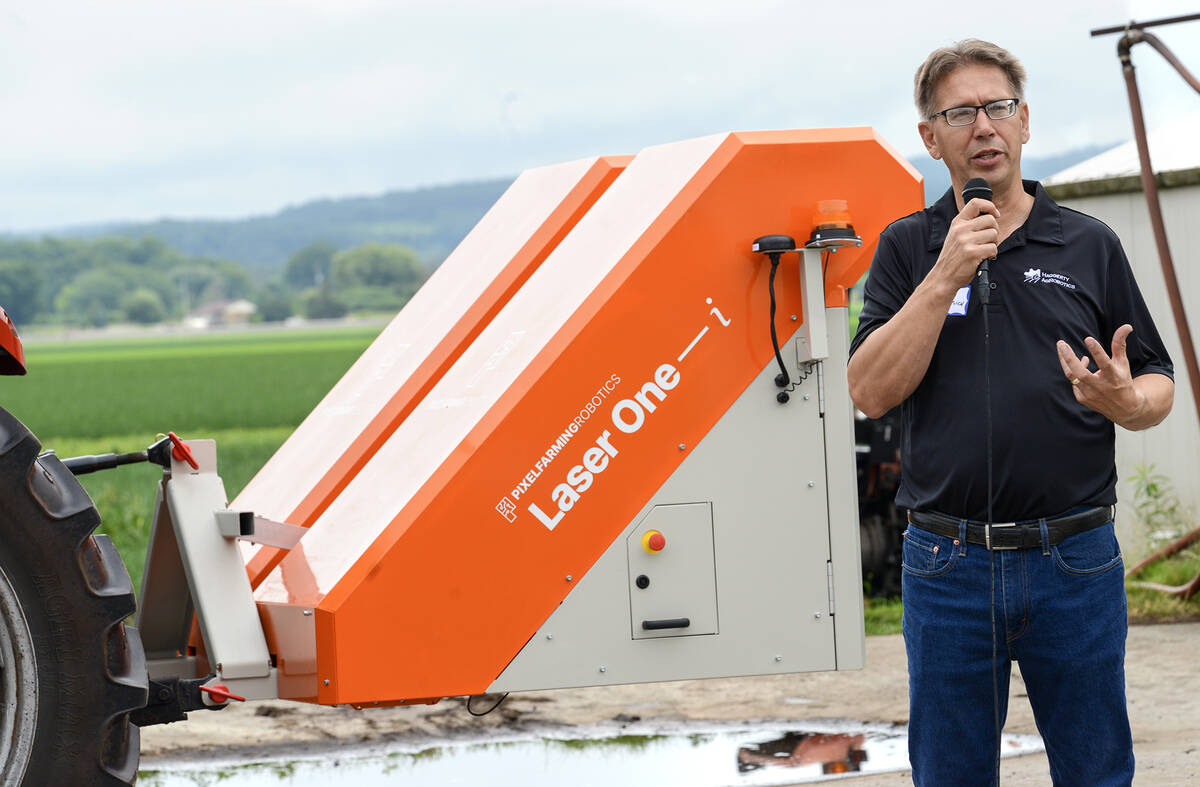 Chuck Baresich, Haggerty AgRobotics, stands beside a bright orange Pixelfarming Laser One–i prototype adapted to fit the Orio NAiO’s frame.