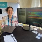 Heather Sanders of AgSenze stands in front of a computer display of her company's system at Ag in Motion 2025.