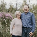 An older couple, Marcel and Laurie Lassaline, stands amidst wildflowers, reflecting on 36 years of farming tradition