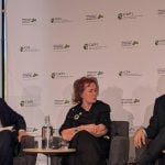 Arlene Dickinson sits between two men on a stage while speaking in a panel discussion.