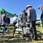 Warren Genick (centre) talks with attendees beside the DJI Agras T100 drone during the drone demonstration at Canada’s Outdoor Farm Show 2025 in Woodstock, Ontario. Photo: Greg Berg
