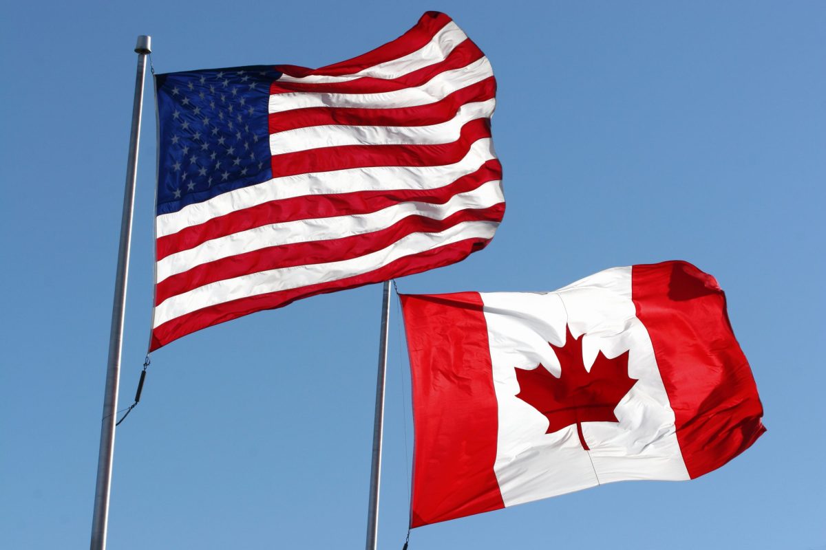 An American and Canadian flag waving in the wind.