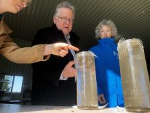 Under the direction of Heather White, Soils at Guelph, far left, Ontario Senator Rob Black, centre, and Yukon Senator Pat Duncan, right, compare the integrity of two soil samples gently laid mesh baskets to see which will hold their form and which will crumble in long tubes of still water.