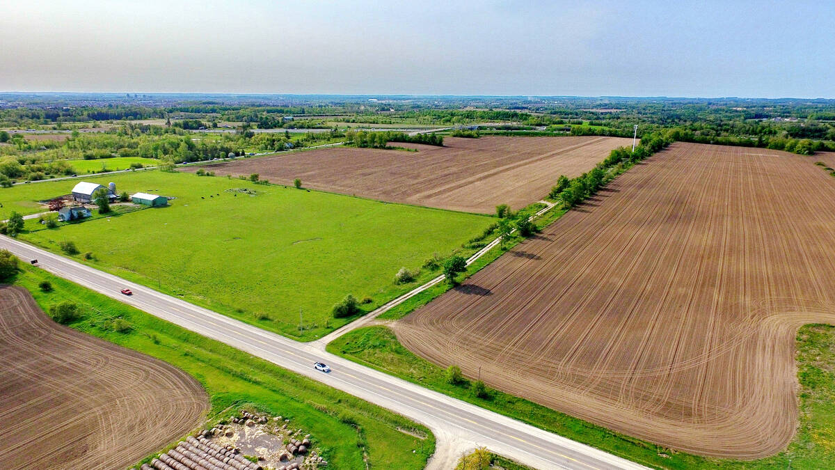 An aerial view of green grass and mostly bare agricultural cropland adjacent to a highway under partly-cloudy blue skies in southern Ontario east of Toronto. Duffins Rouge Agricultural Preserve, Durham County, Ontario, Canada. Spring 2023. Photo: Bob Hilscher/iStock/Getty Images