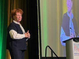Arlene Dickinson speaking on stage at the Grain Farmers of Ontario March Classic, gesturing with one hand, with a large screen behind her.