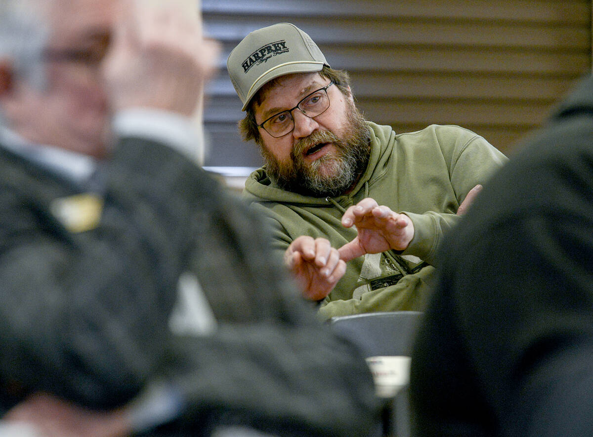 Mark Goetz, a bearded man with dark brown hair, dressed in an army-green sweatshirt and ball cap, gestures with his hands while discussing predation and exemptions to South Bruce&rsquo;s dog bylaw for working livestock and herding dogs to an unseen person. Photo: Diana Martin.