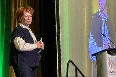 Arlene Dickinson speaking on stage at the Grain Farmers of Ontario March Classic, gesturing with one hand, with a large screen behind her.